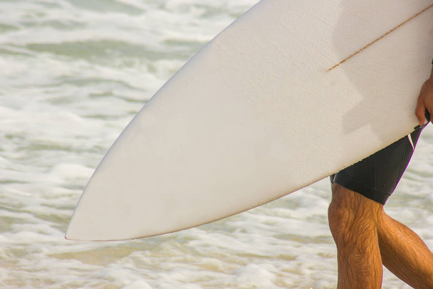 Surfer με ιστιοσανίδα πηγαίνει προς τη θάλασσα στην παραλία Barra da Tijuca στο Ρίο ντε Τζανέιρο. - Φωτογραφία, εικόνα