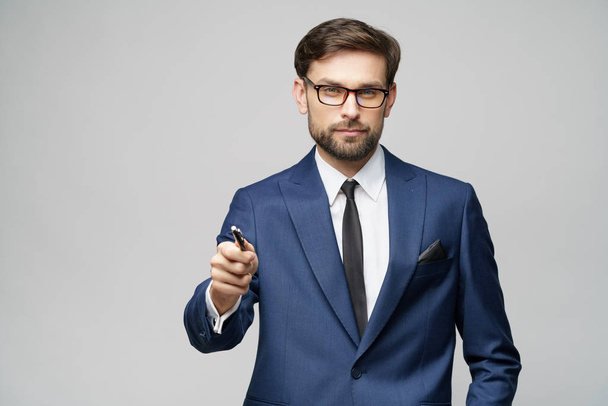 Portrait of a businessman showing pen or pencil at camera over gray background - Foto, Imagem