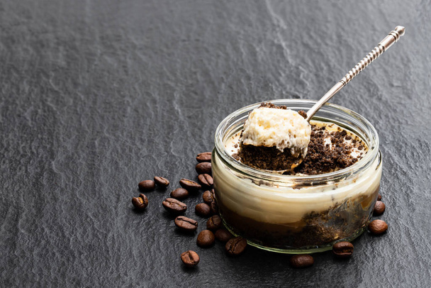 Layered creamy cappuccino cheesecakes in glass jar on black stone background  - Foto, Imagen