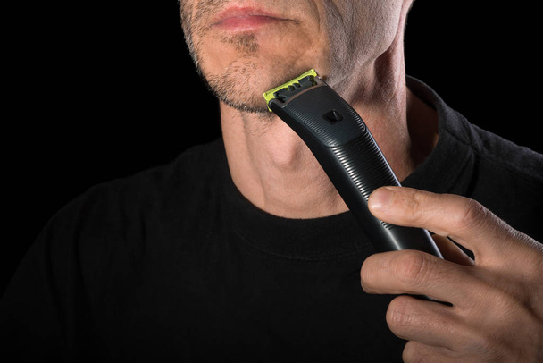  Un homme se rasant le visage avec un rasoir électrique. Gros plan, fond noir
 - Photo, image