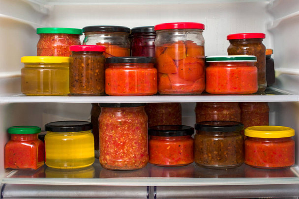 Canned vegetables and jams on refrigerator shelves. - Фото, зображення