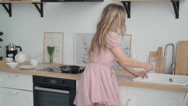girl pours water into a glass from the tap. portrait of a cute girl in the kitchen - Video