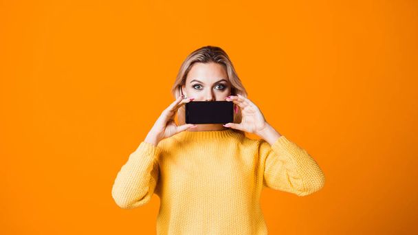 Aranyos fiatal nő egy sárga pulóverben kezében egy okostelefon - Fotó, kép