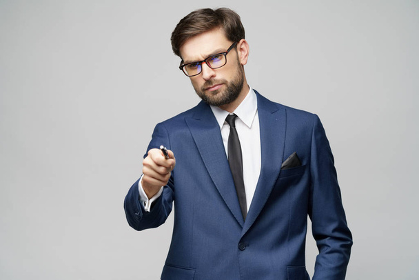 Portrait of a businessman showing pen or pencil at camera over gray background - Fotografie, Obrázek