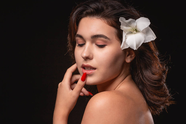 Beautiful woman with bright makeup posing isolated over black background with white flower. - 写真・画像