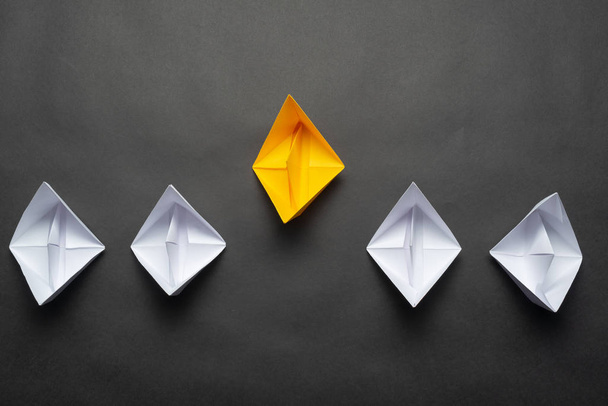 Row of paper ships on black background. Business concept of creative innovation and leadership. Flat lay yellow origami leader boat ahead others boats. Social marketing layout with copy space. - Foto, Imagem
