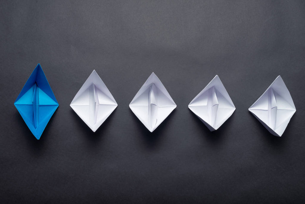 Row of paper ships on black background. Leadership concept with blue paper ship leading among white. Individual motivation and direction. Social marketing layout with copy space. - Foto, Imagem