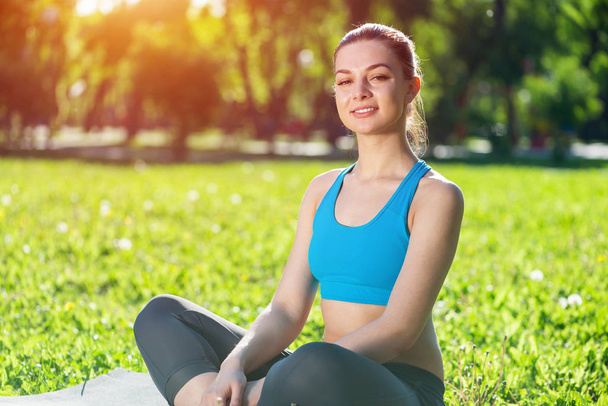Girl meditates in lotus pose on green grass. Practicing of yoga at summer park. Portrait of young peaceful woman. Training and meditation outdoor at summer day. Healthy lifestyle and relaxation. - Photo, Image