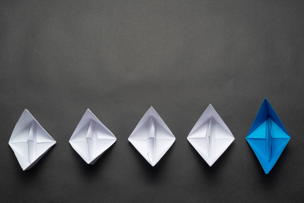 Row of paper ships on black background. Leadership concept with blue paper ship leading among white. Individual motivation and direction. Social marketing layout with copy space. - Фото, зображення