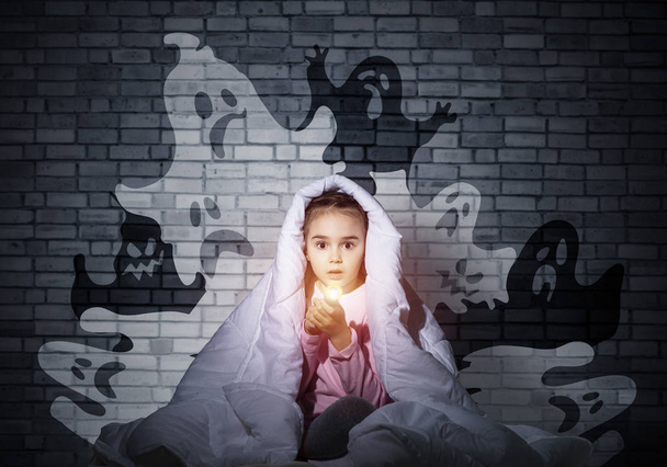 Surprised girl with flashlight hiding under blanket. Amazed kid sitting in his bed at home. Fear of the dark. Little child in pajamas afraid of ghosts at night. Nightmare fantasy and imagination. - Фото, зображення