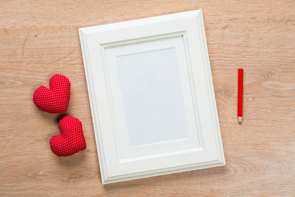 White photo frame small red hearts and pencil on wooden table - Fotografie, Obrázek
