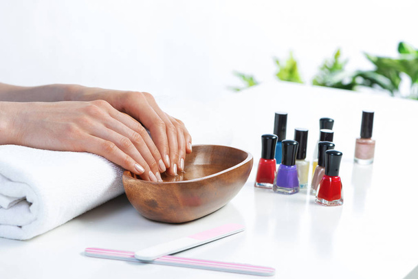 Closeup female hands in wooden bowl with water. Spa procedure and relaxation. Female hands preparing for manicure. Professional nail care and beautician service. Beauty and hygiene concept - Photo, image