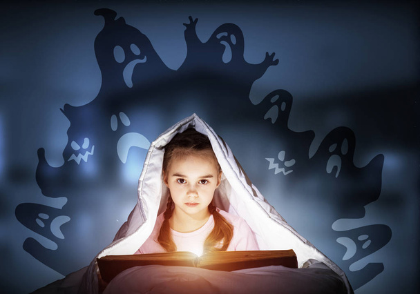 Scared kid with reading book under blanket - Фото, изображение