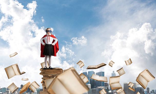 Молодая девушка в костюме супергероя стоит на куче старых книг. Смешанные медиа
 - Фото, изображение