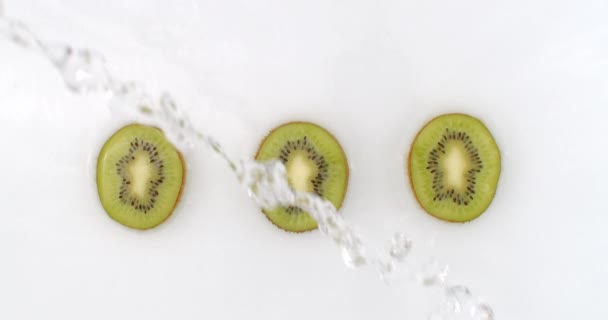 Slow motion water spetteren op drie sneetjes groene kiwi liggend op een witte achtergrond in het water. - Video