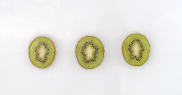 Water spat in slow motion. Bovenaanzicht: drie stukken kiwi gewassen met water op een witte achtergrond. - Video