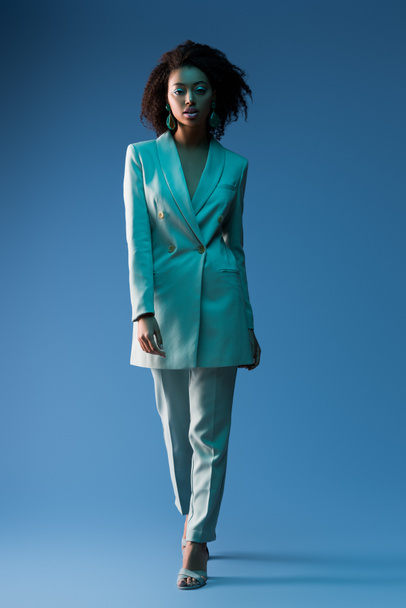  attractive african american woman in suit looking at camera on blue background  - Photo, Image