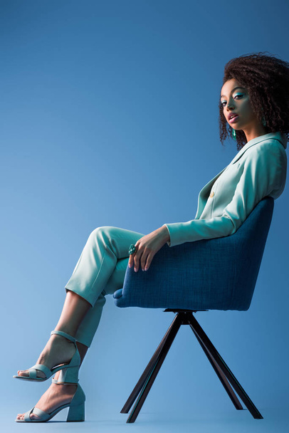 african american woman sitting on armchair on blue background - Фото, зображення