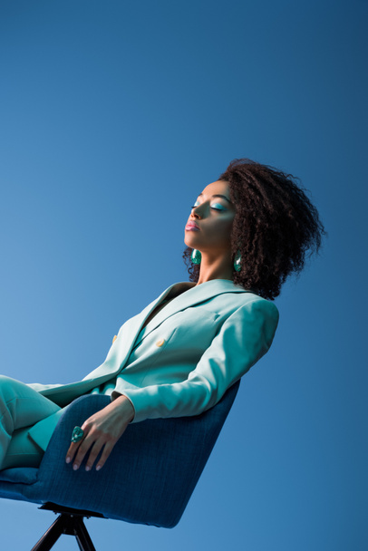 mulher afro-americana sentada em poltrona com os olhos fechados isolados em azul
 - Foto, Imagem