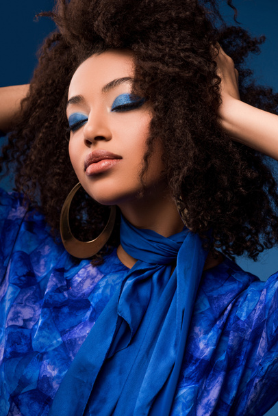 stylish african american woman in dress with closed eyes and makeup isolated on blue  - Fotografie, Obrázek