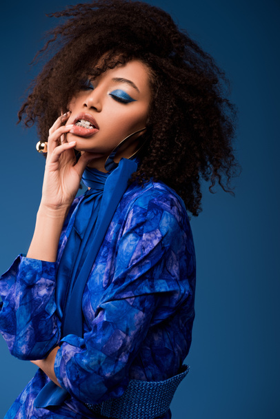 stylish african american woman in dress with closed eyes and makeup isolated on blue  - Foto, Imagen