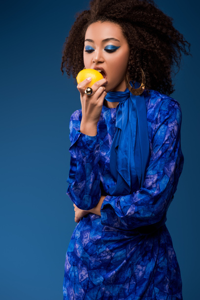 african american woman eating tasty lemon isolated on blue - Foto, imagen