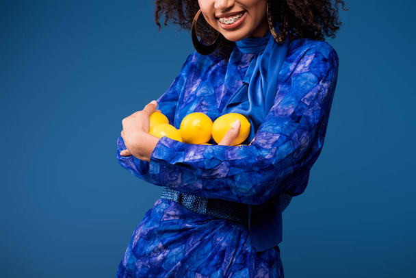 levágott kilátás mosolygós afro-amerikai nő gazdaság citrom elszigetelt kék  - Fotó, kép