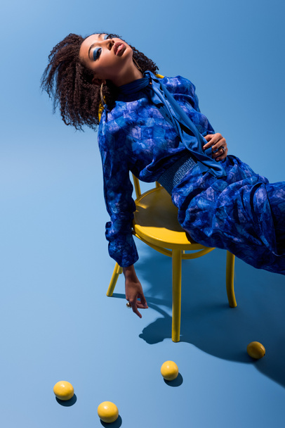 african american woman sitting on chair on blue background  - Фото, зображення