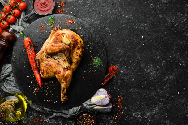 Baked quail, chicken with chili pepper on a black stone plate. Top view, free space for your text. Rustic style. - Foto, Bild