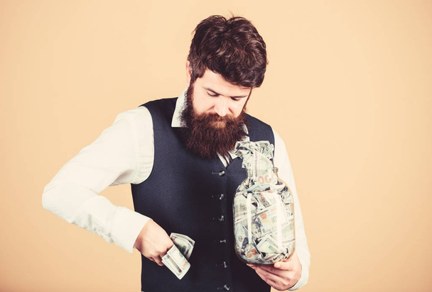 Pocketing company savings. Bearded man taking money savings out of glass jar. Businessman stealing business savings. Making life savings for future - Foto, imagen