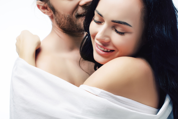 feliz sexy pareja abrazándose en blanco sábanas, aislado en blanco
 - Foto, Imagen