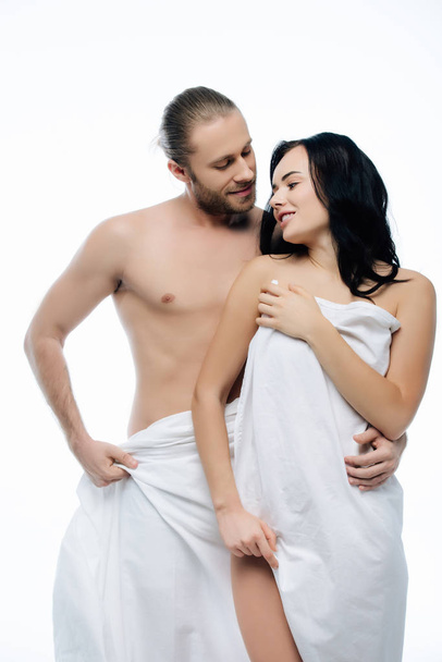 Nacktes junges Paar, das sich in weißen Laken umarmt, isoliert auf weiß - Foto, Bild