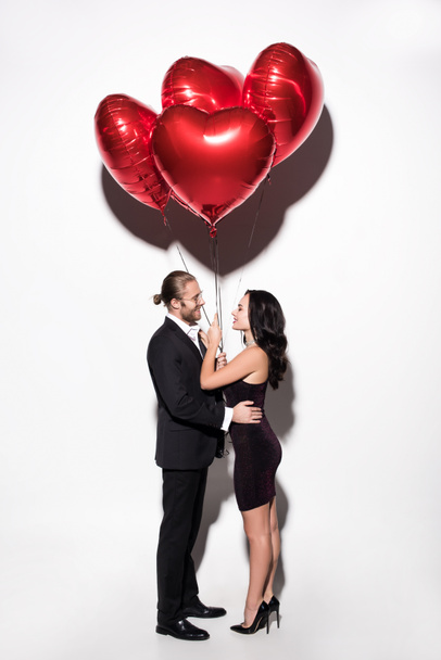 beautiful happy couple holding red heart shaped balloons on valentines day on white - Foto, imagen