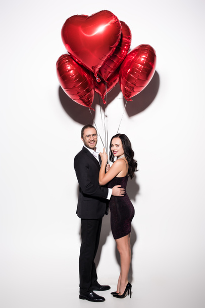 smiling couple holding red heart shaped balloons on valentines day on white - Foto, imagen