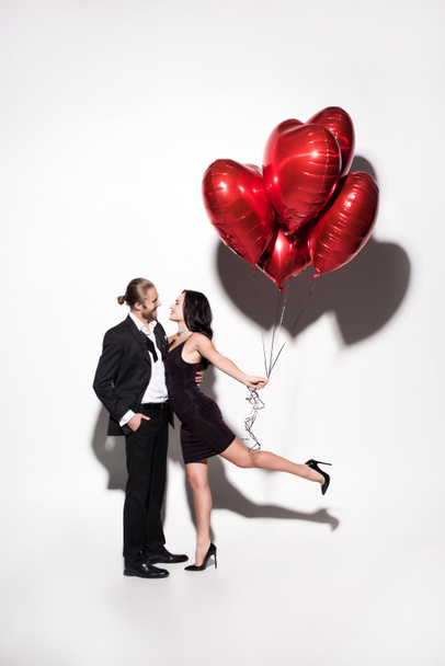 smiling couple holding red heart shaped balloons on valentines day on white - Fotoğraf, Görsel