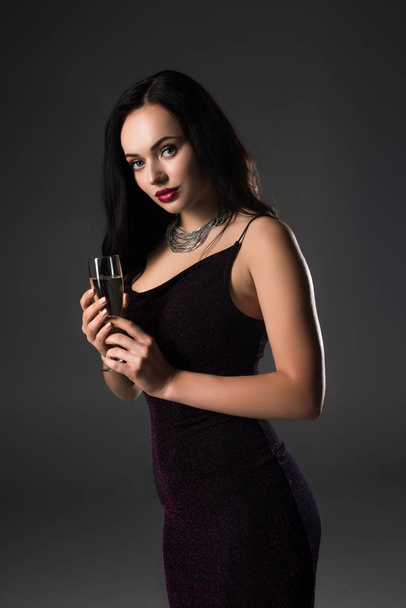 attractive girl in black dress holding glass of champagne, isolated on grey - Foto, afbeelding