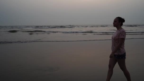mladá žena kráčí po pláži při západu slunce - Záběry, video