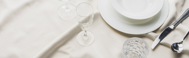 Hochwinkelaufnahme von Geschirr mit Besteck und Gläsern auf weißer Tischdecke, Panoramaaufnahme - Foto, Bild