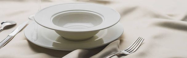 Panoramic shot of plates and cutlery on wavy white tablecloth - Photo, Image