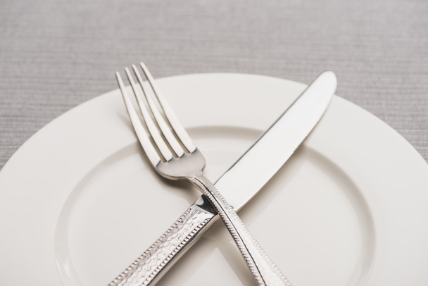 Close up view of fork and knife on empty plate on grey surface - Photo, image