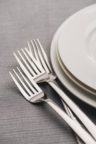 Tenedores brillantes al lado de servir platos en mantel gris
 - Foto, imagen