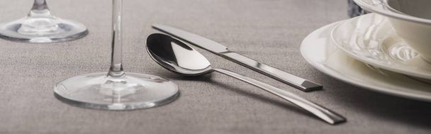 Cuchara y tenedor junto a copas de vino y platos en tela gris, plano panorámico
 - Foto, imagen