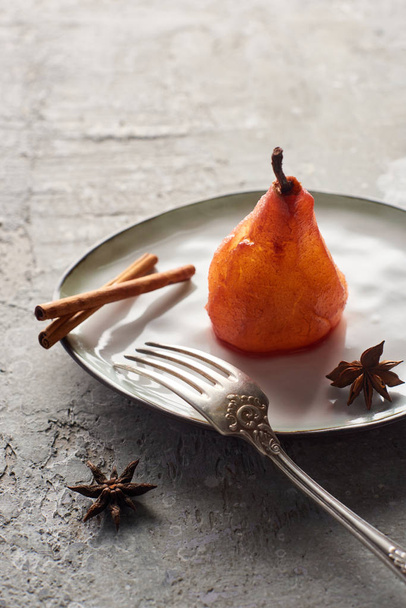 delicious pear in wine with cinnamon and anise on plate with silver fork on grey concrete surface - Foto, Imagen