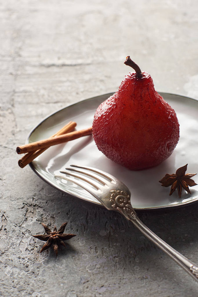 delicious pear in wine with cinnamon and anise on plate with silver fork on grey concrete surface - Foto, immagini