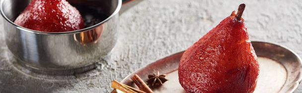 νόστιμο αχλάδι σε κρασί σε κατσαρόλα και σε ασημένιο πιάτο με κανέλα και γλυκάνισο σε γκρι τσιμεντένια επιφάνεια, πανοραμική λήψη - Φωτογραφία, εικόνα