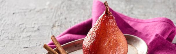 delicious pear in wine with cinnamon on silver plate on grey concrete surface with pink napkin, panoramic shot - Photo, Image
