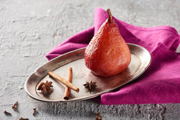 delicious pear in wine with cinnamon and anise on silver plate on grey concrete surface with pink napkin - Foto, afbeelding