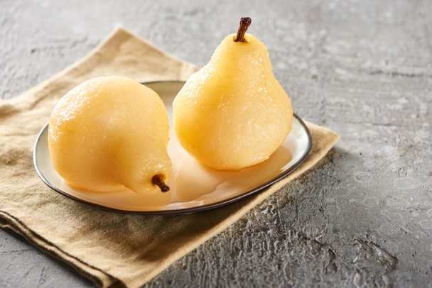 delicious pear in wine served on plate on napkin on grey concrete surface - Photo, Image