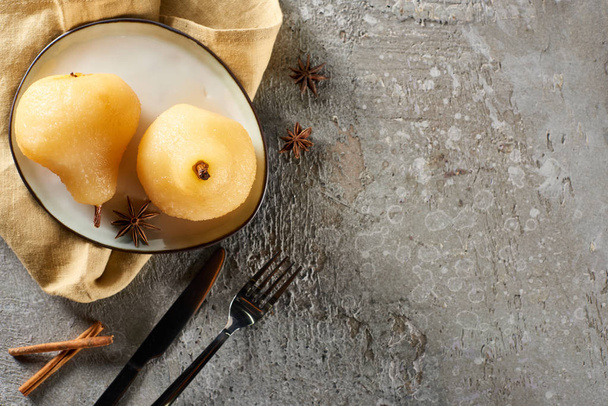 ylhäältä näkymä herkullinen päärynä viiniä anis ja kaneli tarjoillaan lautasella lautasliina veitsi ja haarukka harmaalla betonipinnalla
 - Valokuva, kuva