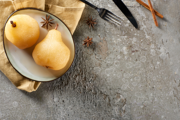 ylhäältä näkymä herkullinen päärynä viiniä anis ja kaneli tarjoillaan lautasella lautasliina veitsi ja haarukka harmaalla betonipinnalla
 - Valokuva, kuva